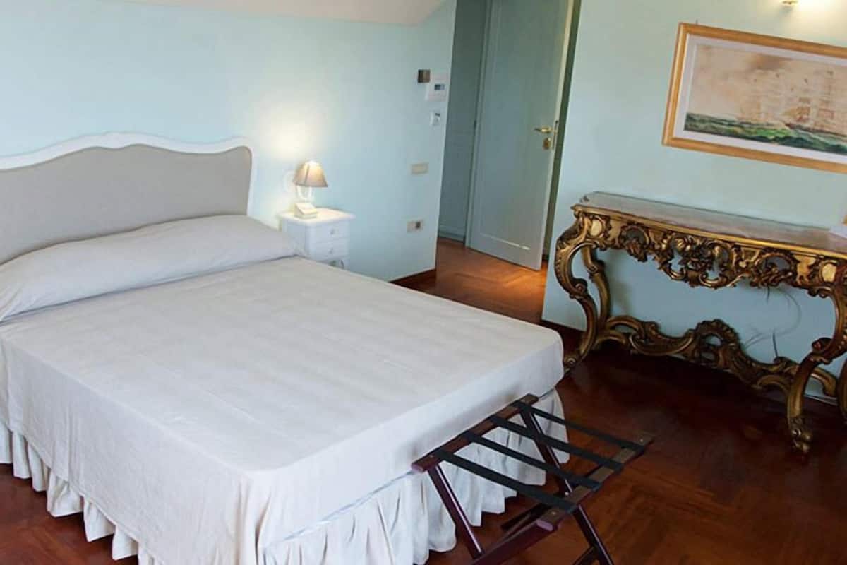 A bedroom with a large bed, bedside tables with lamps, a wooden floor, and a decorative console table.