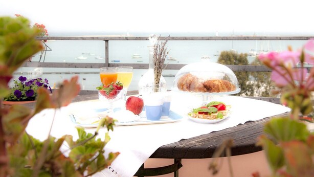 Una mesa con un desayuno que incluye croissants, una ensalada de frutas y jugo, con vista a un puerto deportivo.