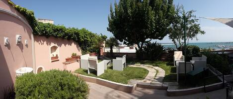 Un patio con mobiliario exterior, un árbol grande y vista al mar.