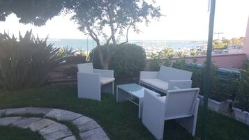 A patio with wicker furniture, a small table, and a view of the sea and boats in the background.