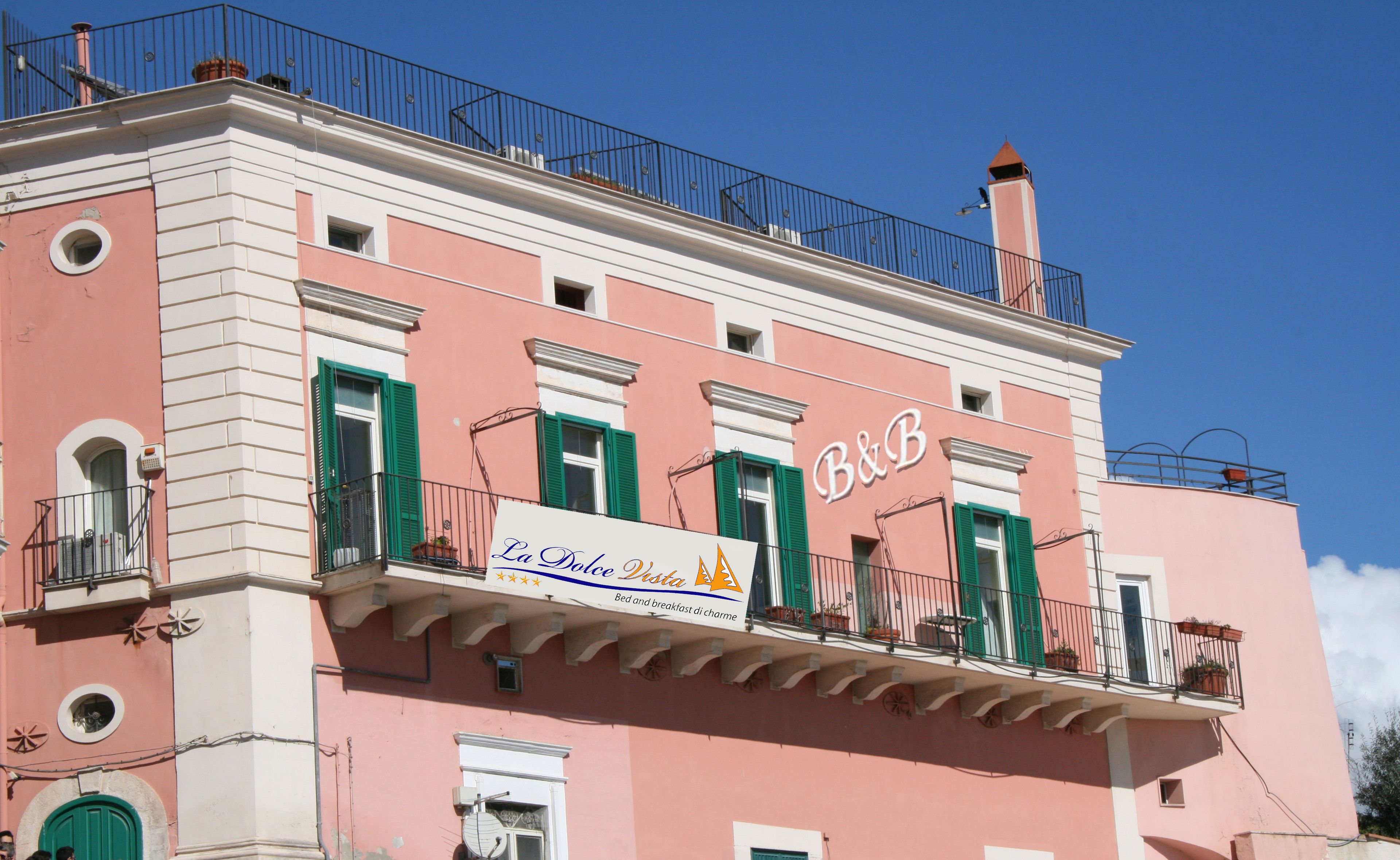 Ein rosafarbenes Gebäude mit Balkonen und einem Schild für "La Dolce Vita Bed and breakfast di charme".