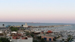 Un puerto costero con numerosas embarcaciones amarradas, un faro destacado y un puente al fondo.