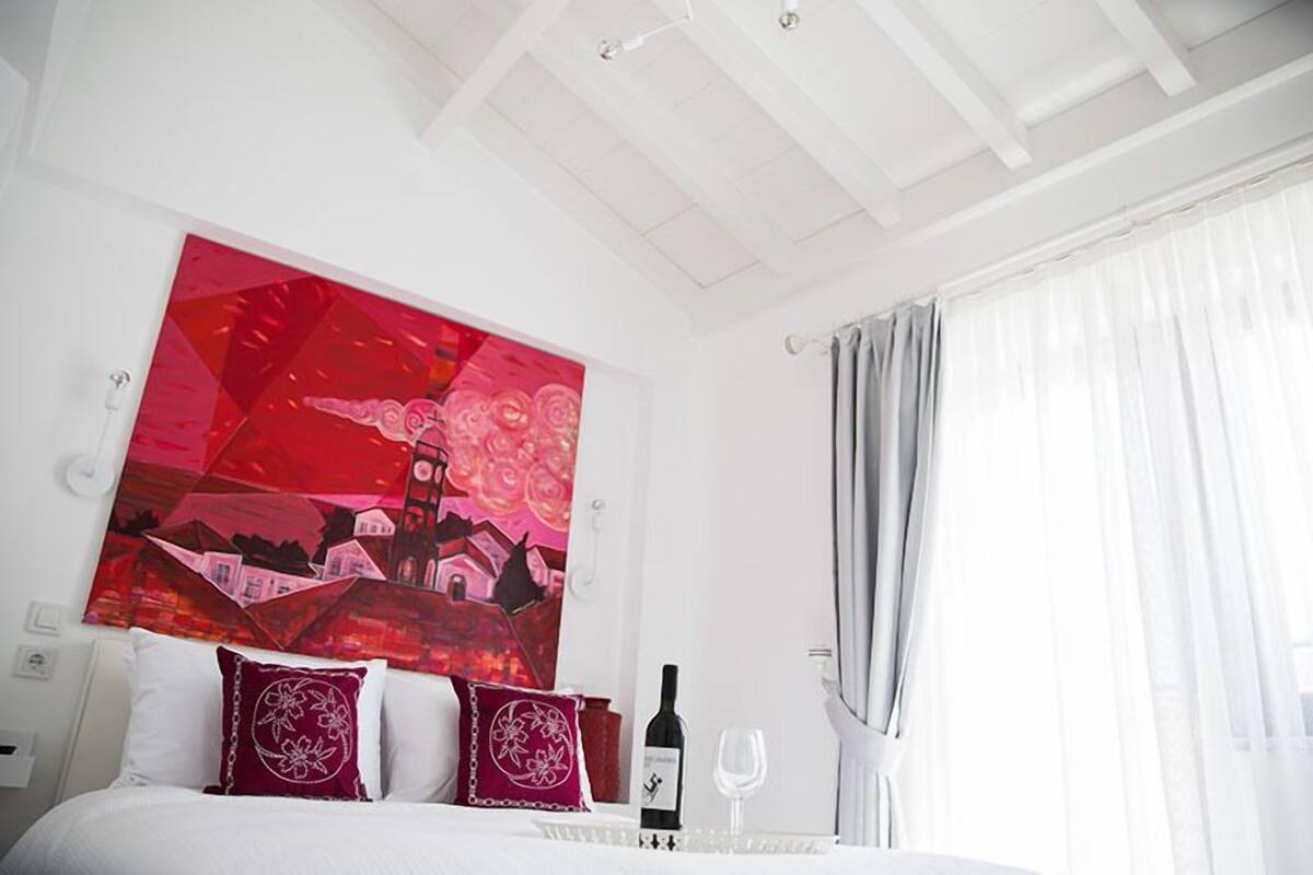 Habitación de hotel con una cama, un cuadro abstracto grande en la pared, una botella de vino y una copa sobre la mesita de noche.
