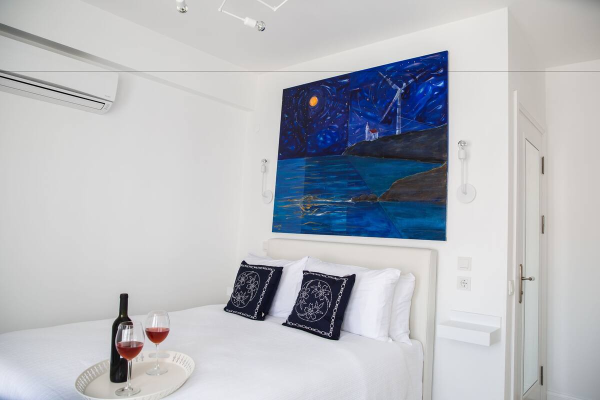 Un dormitorio con cama, un cuadro de una escena nocturna, una botella de vino y dos copas sobre una bandeja.