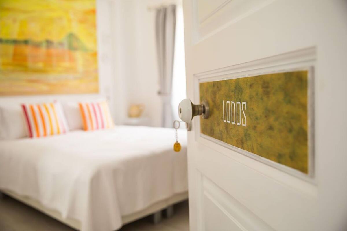 Una habitación de hotel con una cama, una puerta con la etiqueta 'LODOS' y un cuadro en la pared.