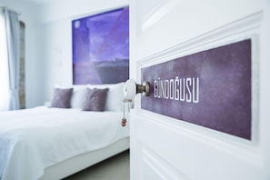 A hotel room with a bed, a door with a sign, and a large window with a view. - Esinti Hotel (Bozcaada)