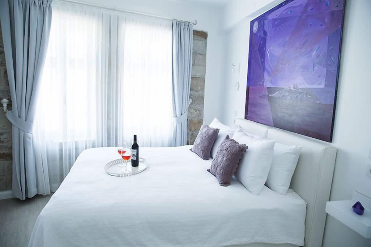 Una habitación de hotel con una cama, un cuadro en la pared y una ventana con cortinas.
