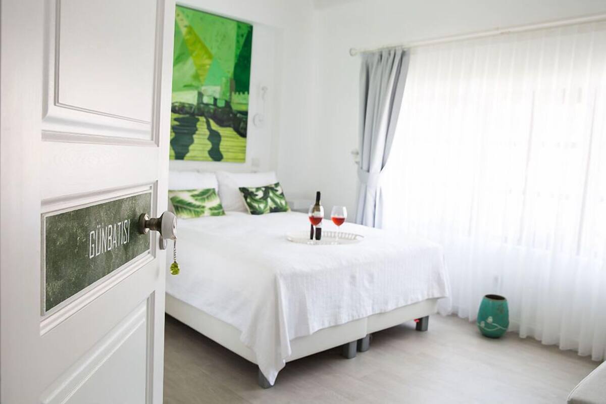 Un dormitorio ordenado con cama, mesita de noche, un jarrón verde y un cuadro en la pared.