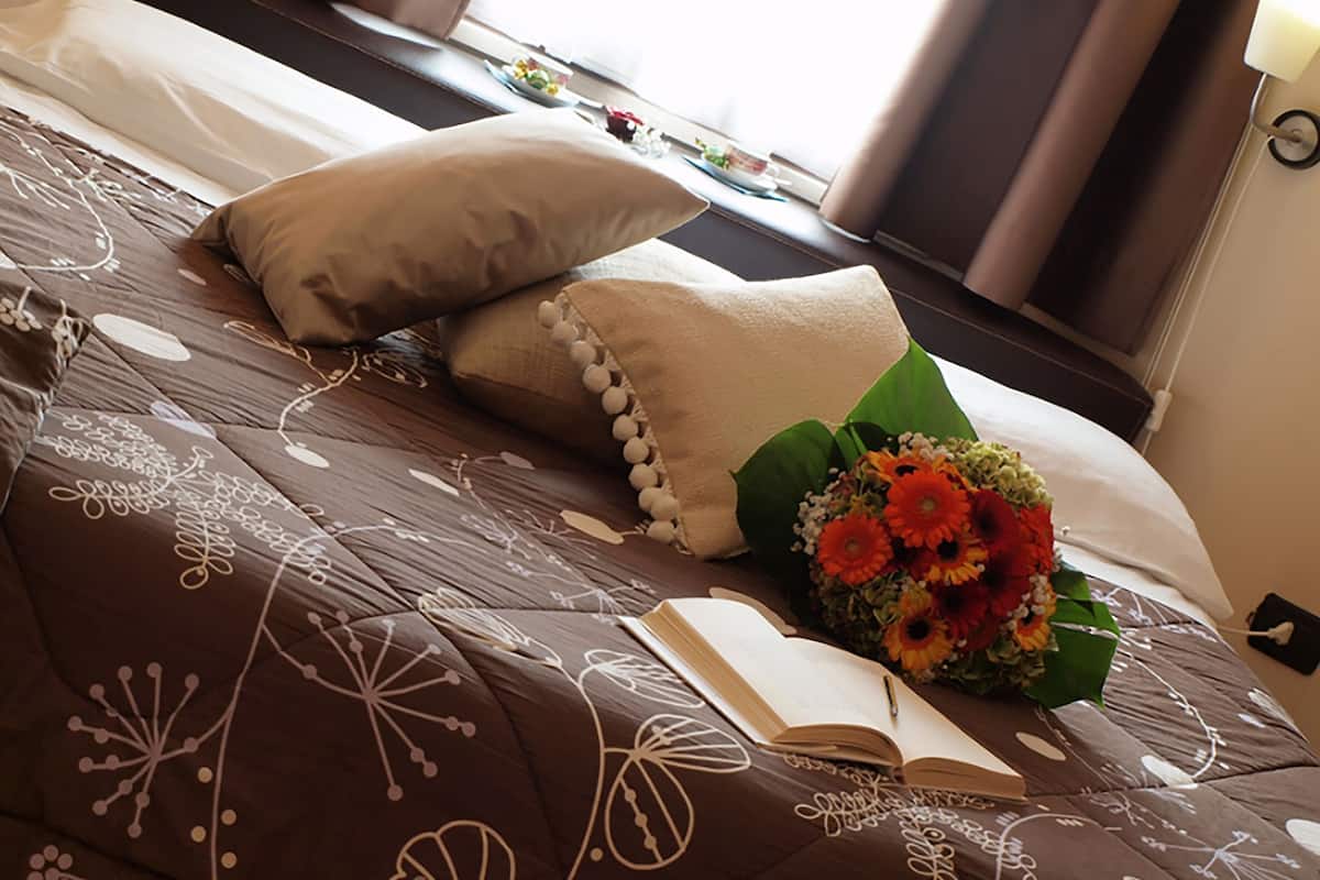 A neatly made bed with a brown patterned bedspread, a bouquet of flowers, and an open book on the bed.