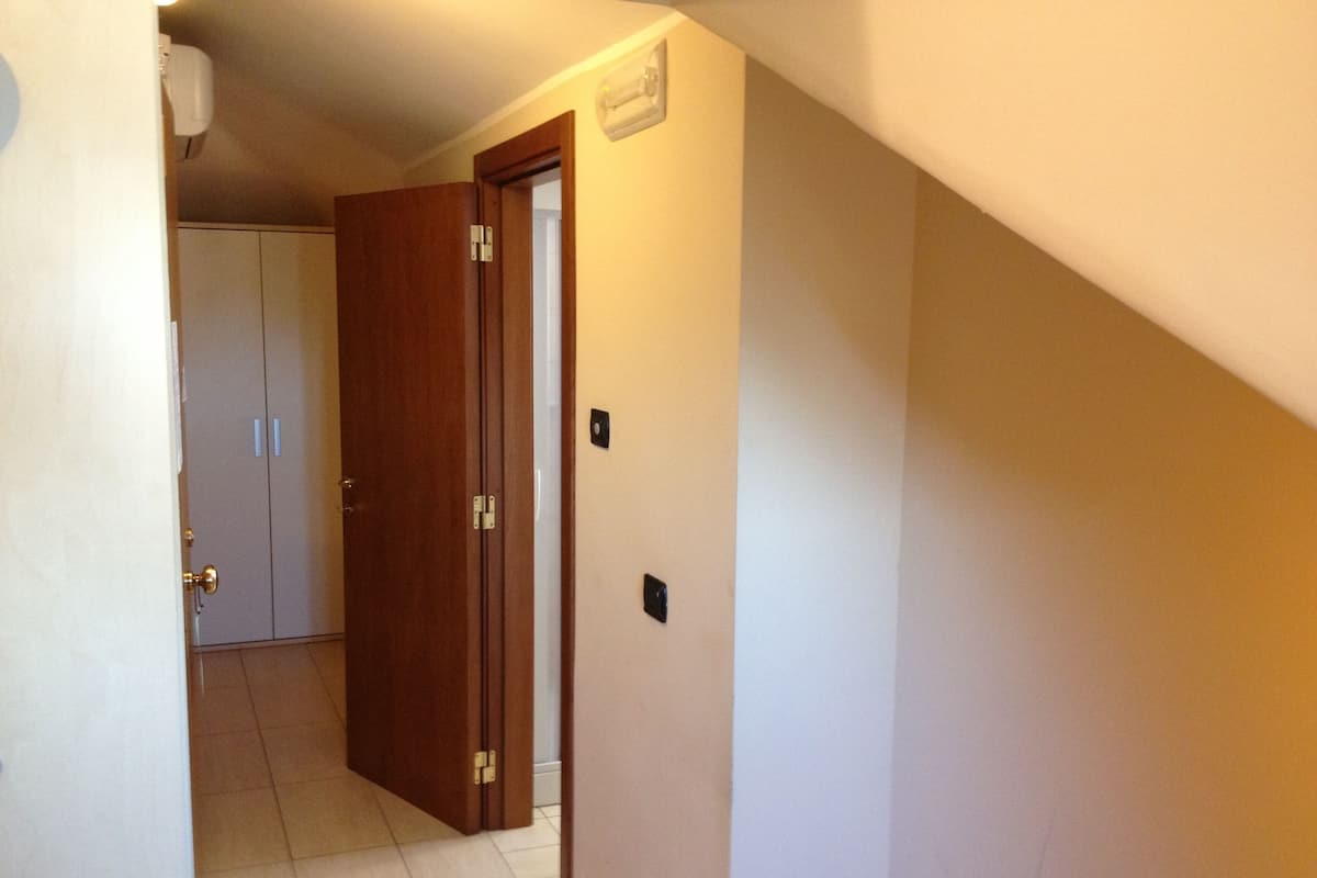 A hallway with a wooden door, a white wall, and a tiled floor.