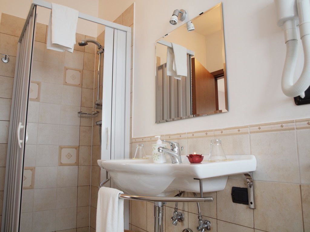A bathroom with a glass-enclosed shower, a white sink with a soap dispenser, and a mirror above the sink.