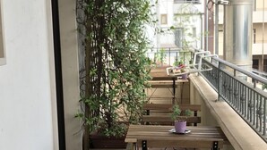 A narrow balcony with two wooden tables and chairs, a potted plant, and a metal railing.