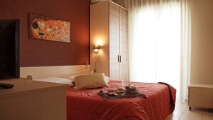 A hotel room with a bed, a desk, a lamp, a painting on the wall, and a window with curtains.