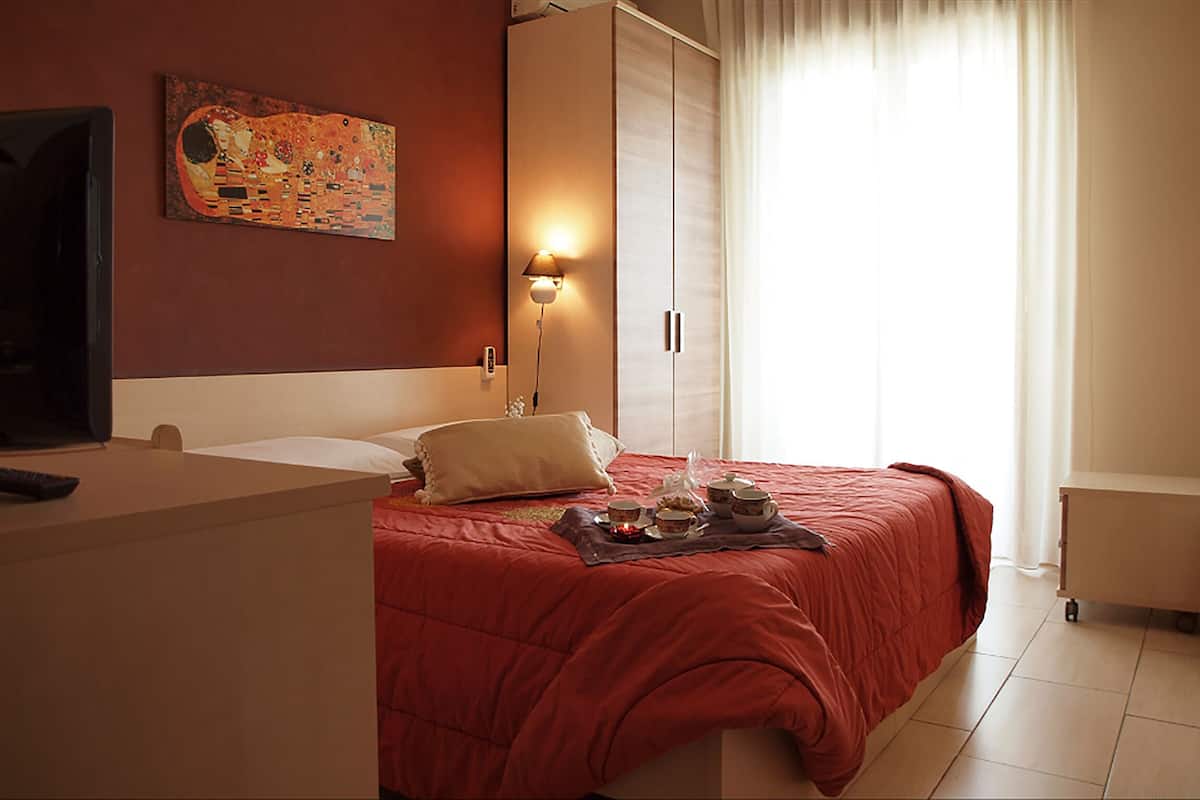 A hotel room with a bed, a desk, a lamp, a painting on the wall, and a window with curtains.