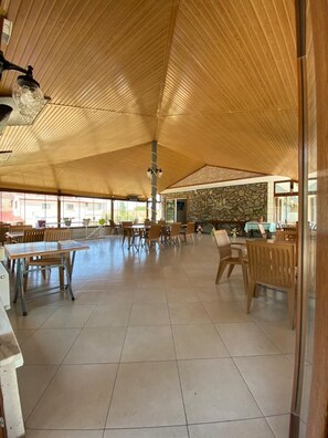 An indoor dining area with wooden tables and chairs, a stone wall, and a tiled floor. - Geyikli Berfin Otel (Ezine)