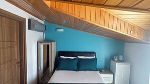 A bedroom with a wooden ceiling, a bed with teal bedding, a small white bedside table, and a white wardrobe. - Geyikli Berfin Otel (Ezine)
