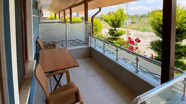 A balcony with a wooden ceiling, a table with chairs, and a view of greenery and buildings. - Geyikli Berfin Otel (Ezine)