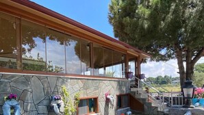 A modern house with a stone facade, large windows, and a staircase leading to a covered porch. - Geyikli Berfin Otel (Ezine)