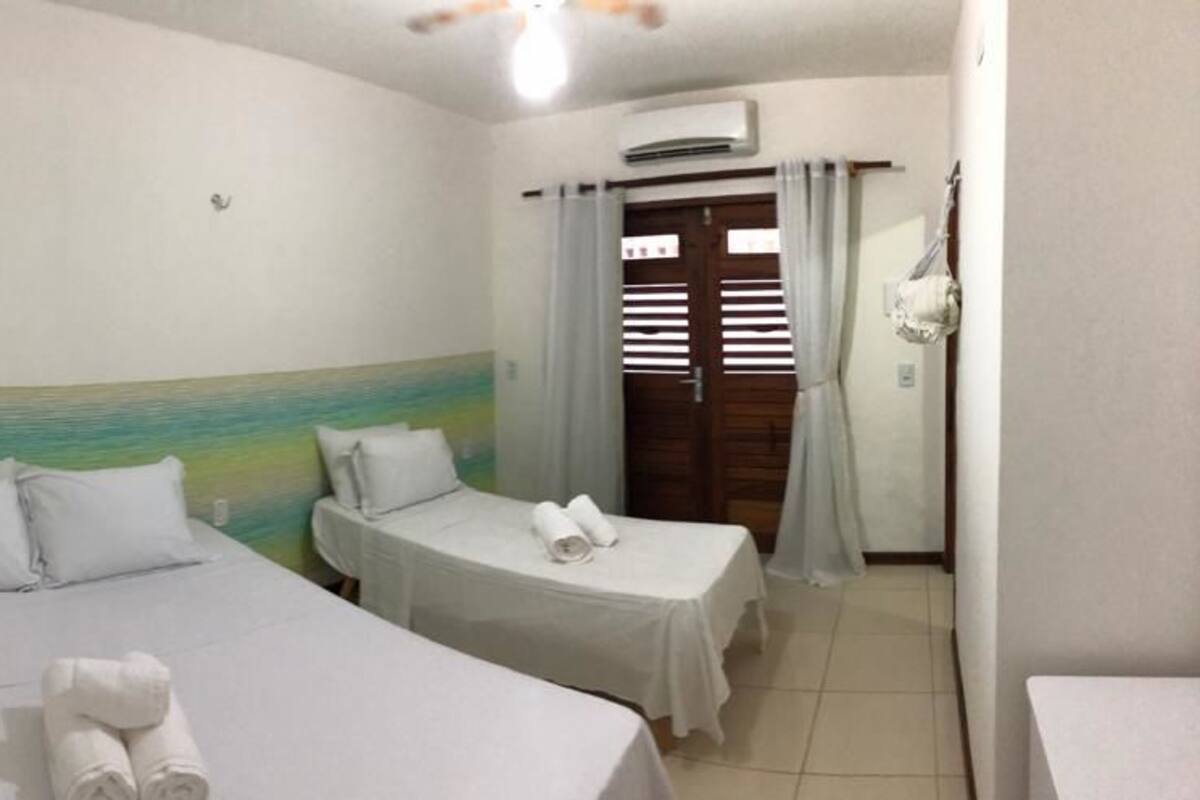 Una habitación con dos camas individuales, ventilador de techo, aire acondicionado y una puerta de madera con cortinas.