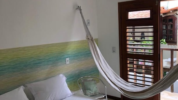 A single bed with a green bedspread, white pillows, and a white blanket rolled up at the foot. A hammock is tied to the headboard. - Pousada A Casa é Sua (Jijoca de Jericoacoara)