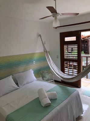 Ein Einzelbett mit einer grünen Bettdecke, weißen Kissen und einer am Fuß hochgerollten weißen Decke. Eine Hängematte ist an der Kopfteil befestigt.