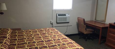 Una habitación de hotel con cama, escritorio, silla, unidad de aire acondicionado y ventana.