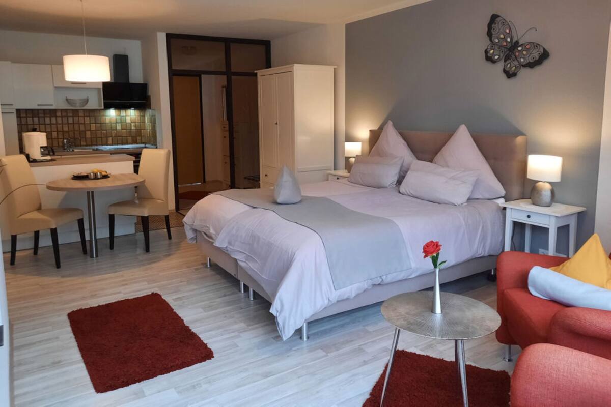 Une chambre d’hôtel moderne avec un lit, une petite table à manger, une chaise rouge, un tapis rouge et une décoration murale représentant des papillons.