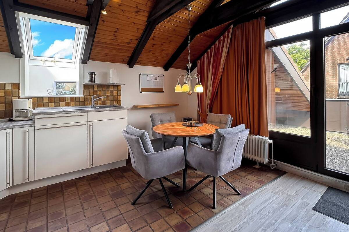 Une cuisine moderne avec un coin repas, des poutres apparentes en bois au plafond et une vue dégagée grâce à de grandes fenêtres.