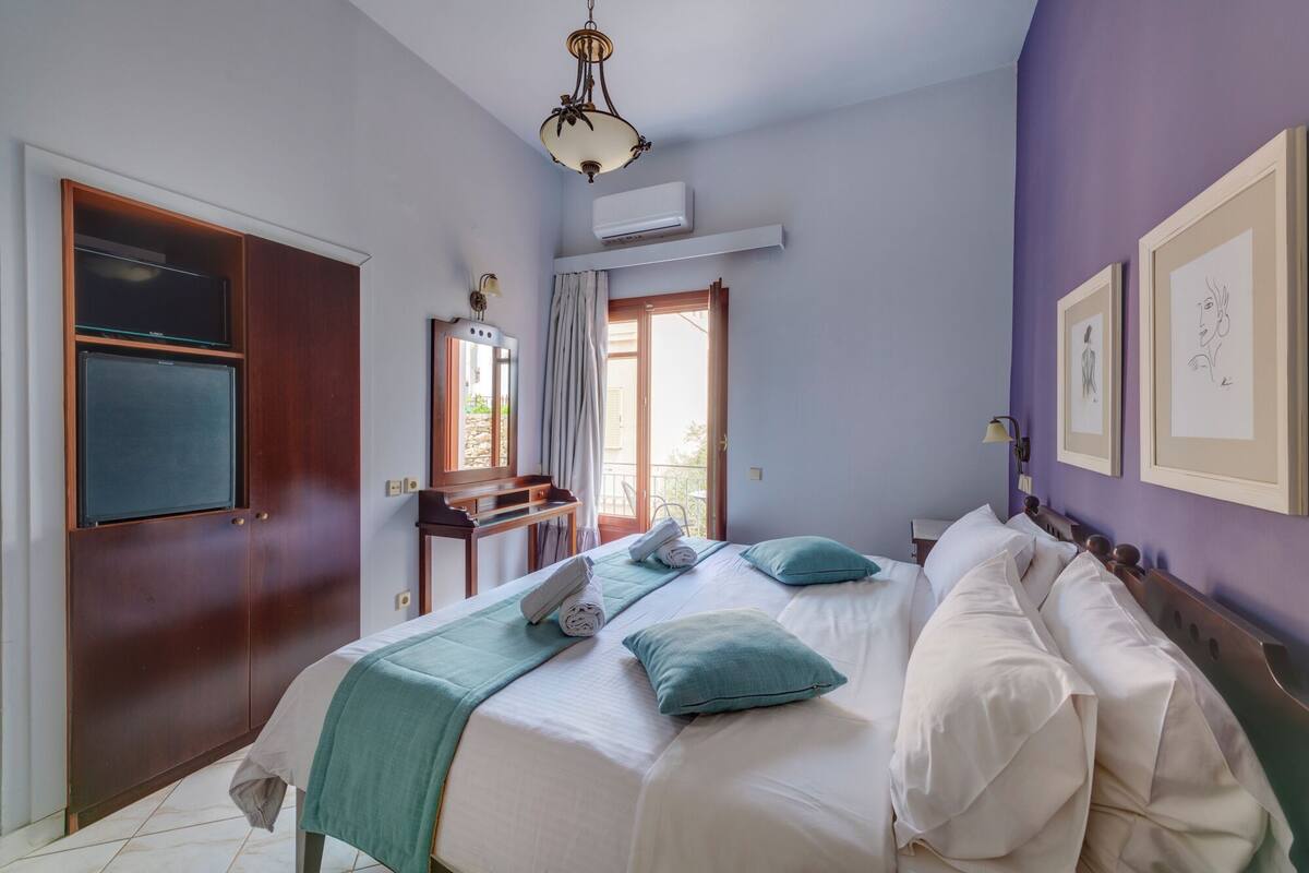 A bedroom with a bed, a desk, a mirror, and a window.