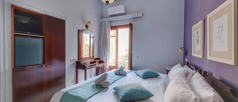 A bedroom with a bed, a desk, a mirror, and a window.