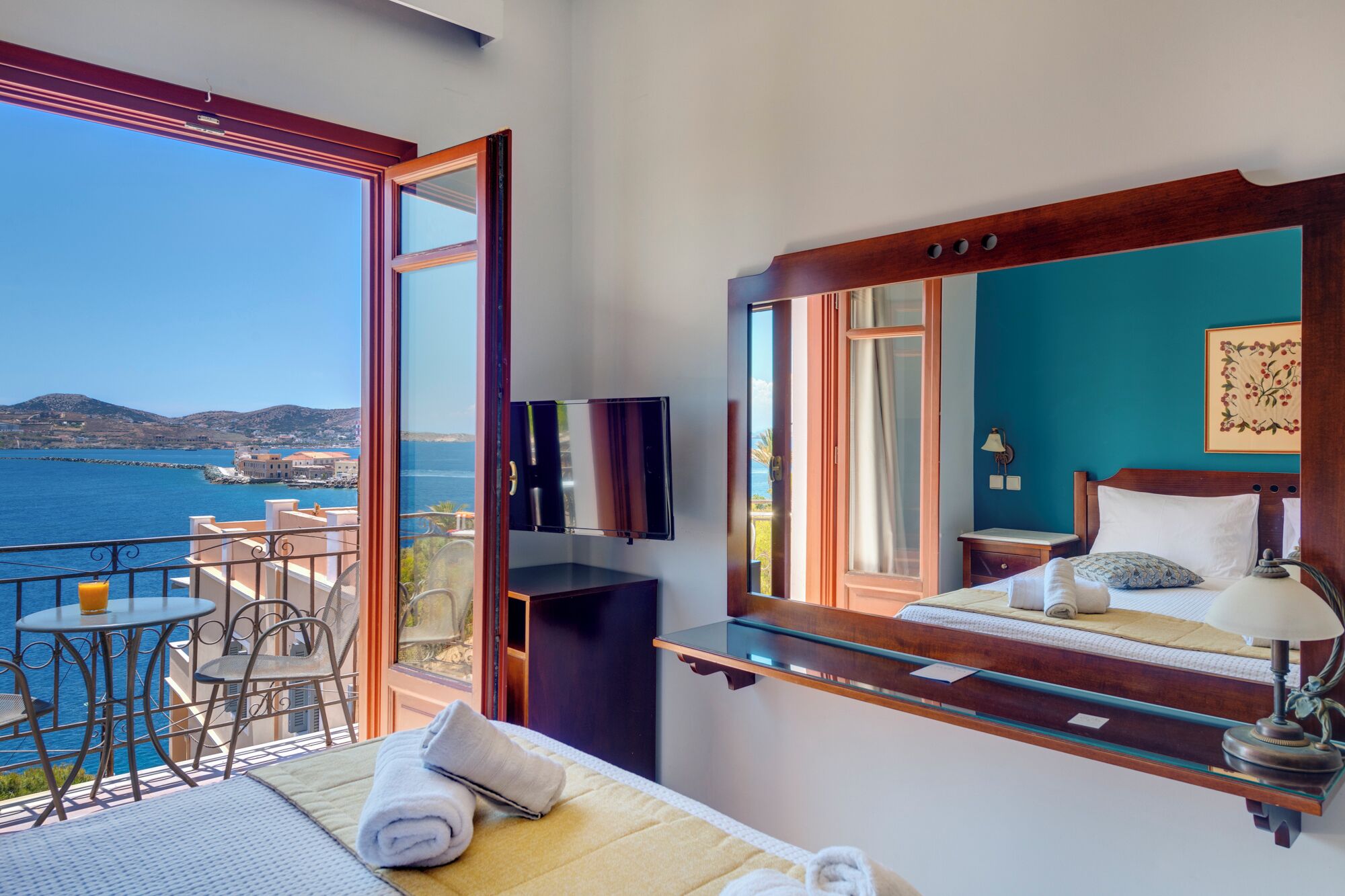 A balcony with a table and chairs, a bed with a nightstand, and a large mirror.