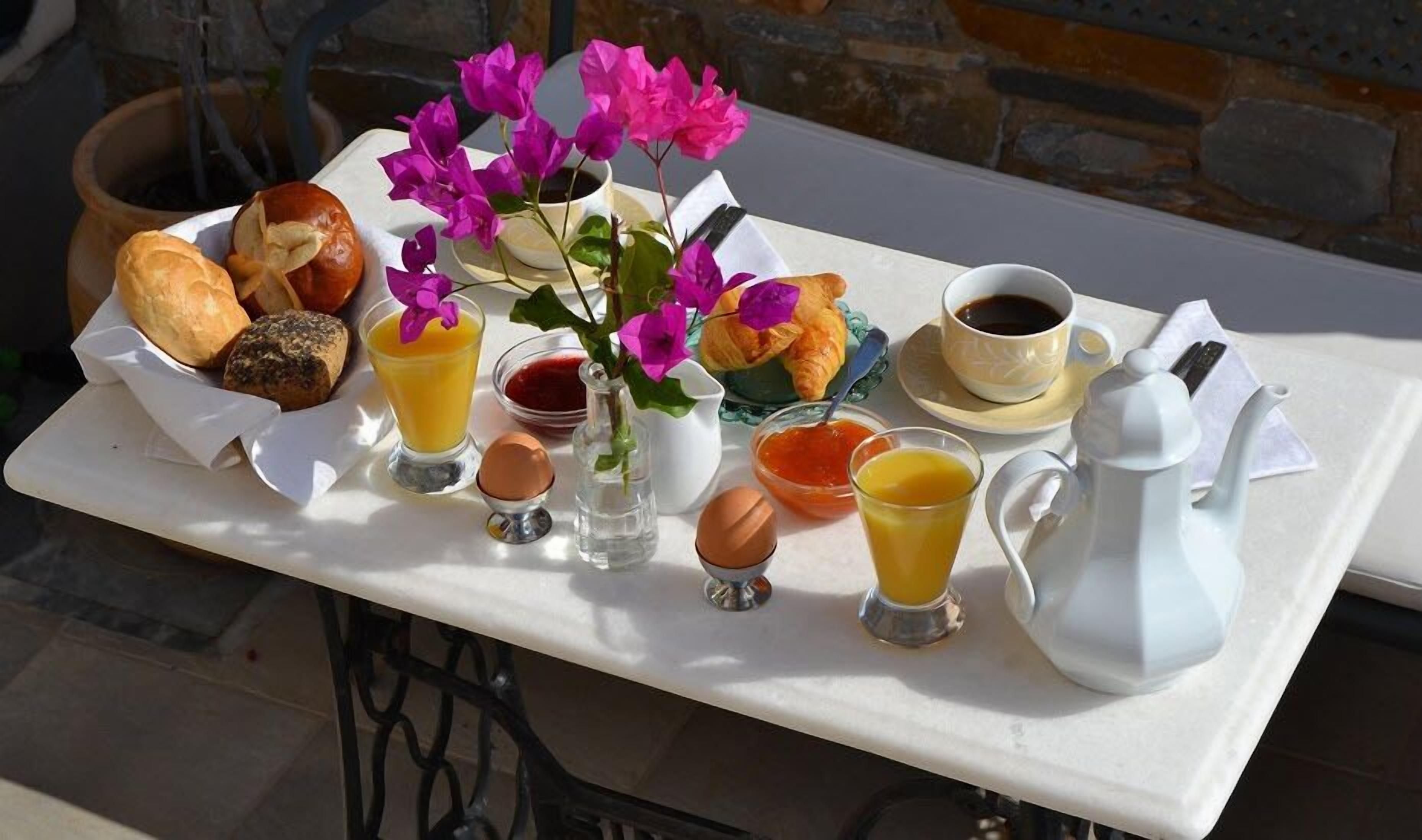 En bakke med morgenmad, bestående af croissanter, brød, æg, appelsinjuice, marmelade og en tepotte.