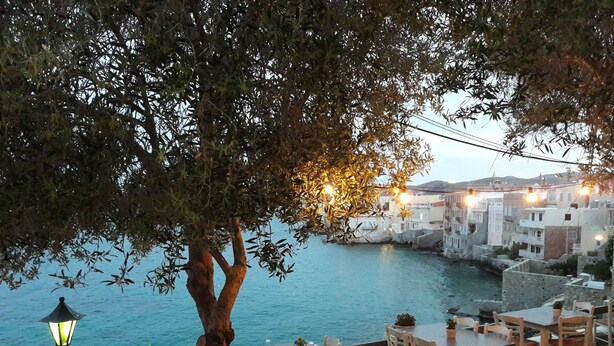 A seaside restaurant with outdoor seating overlooking a body of water and a historic town in the background. - Electra Syros Boutique Hotel (Syros)