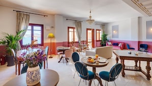 A spacious hotel dining area with multiple round tables, comfortable seating, and a view of the sea. - Electra Syros Boutique Hotel (Syros)