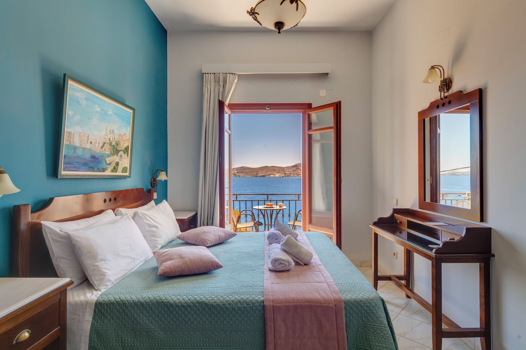 Habitación de hotel con cama, escritorio, silla, un cuadro y vista al mar.