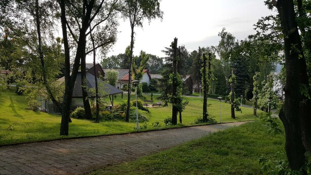 A pathway leading through a park with trees and a building in the background. - Centrum Wypoczynku Odys (Tresna)