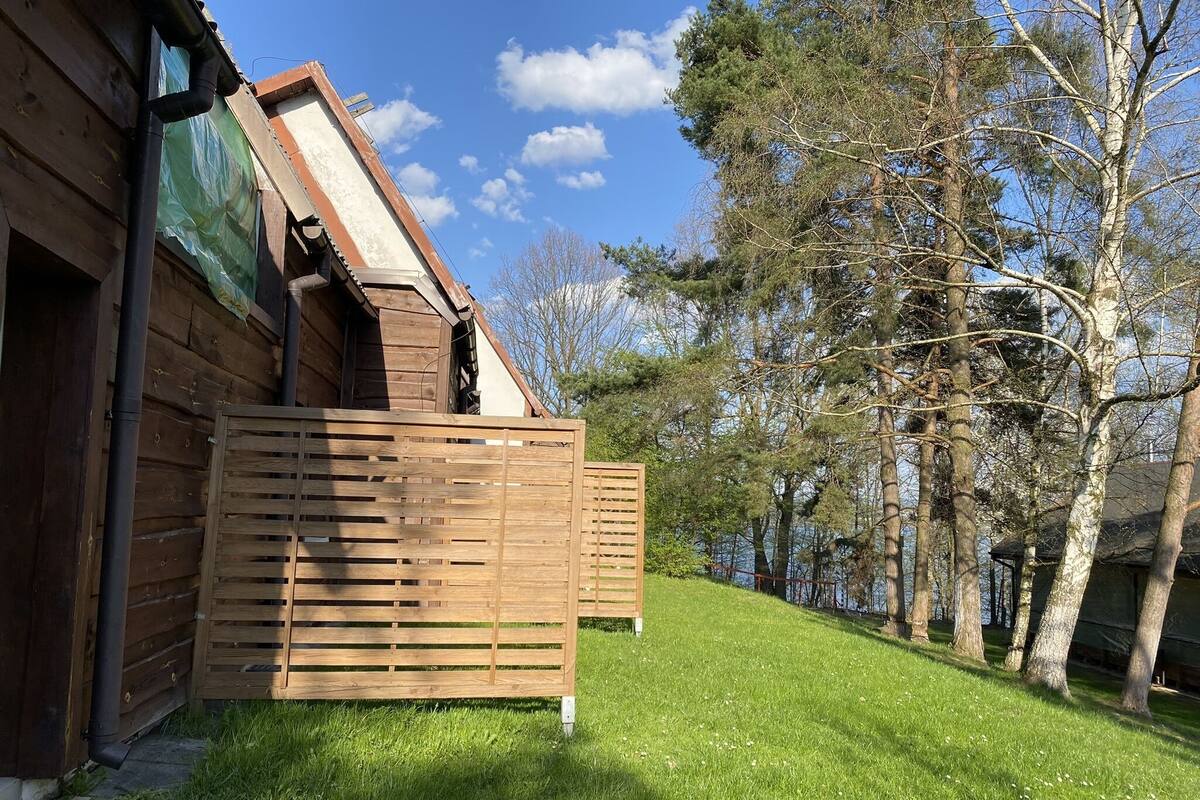 A wooden cabin with a sloped roof, a wooden fence, and a grassy yard.