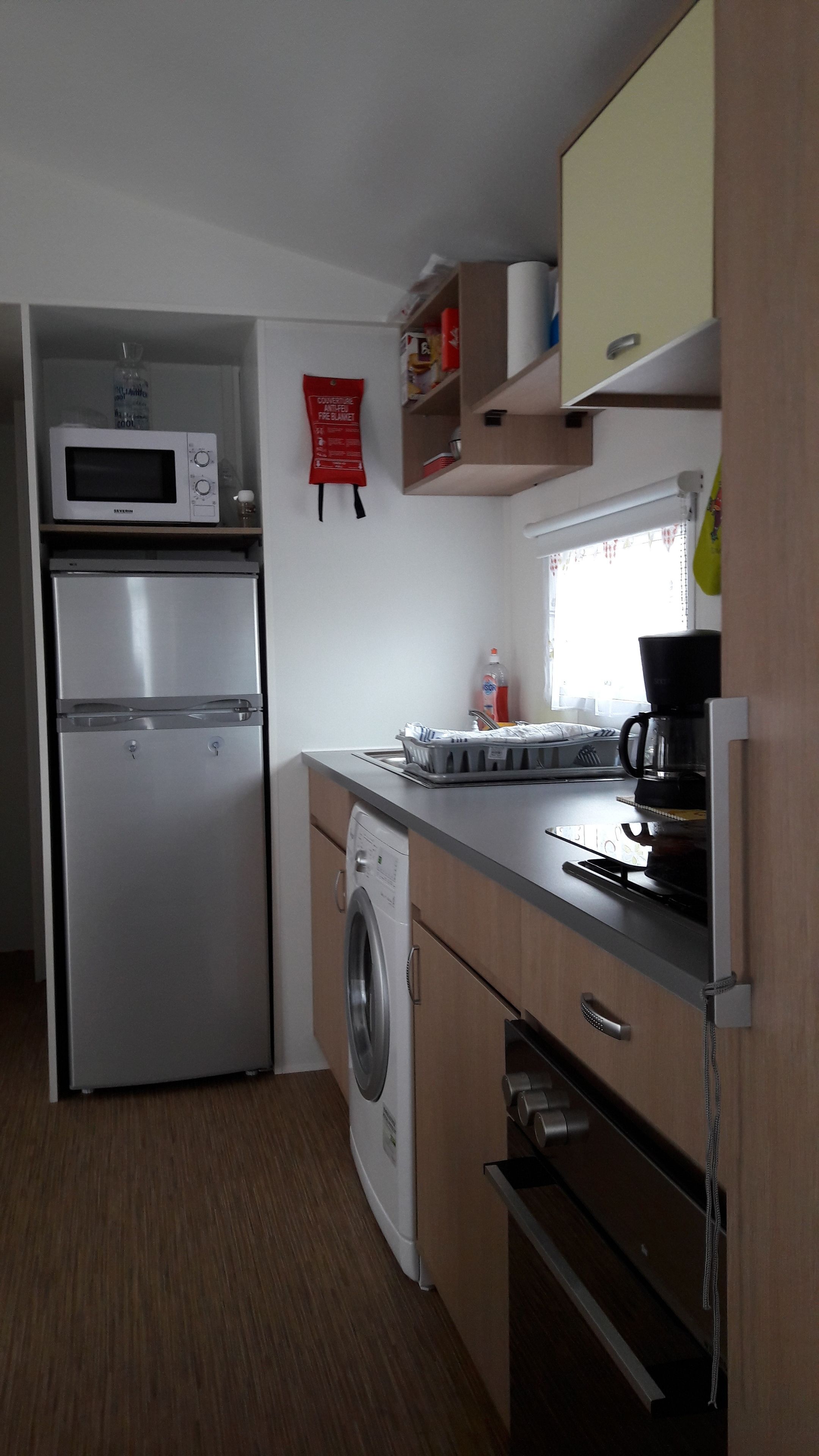 Eine kompakte Küche mit einem Edelstahl-Kühlschrank, einer Mikrowelle, einer Waschmaschine und einer Kaffeemaschine.