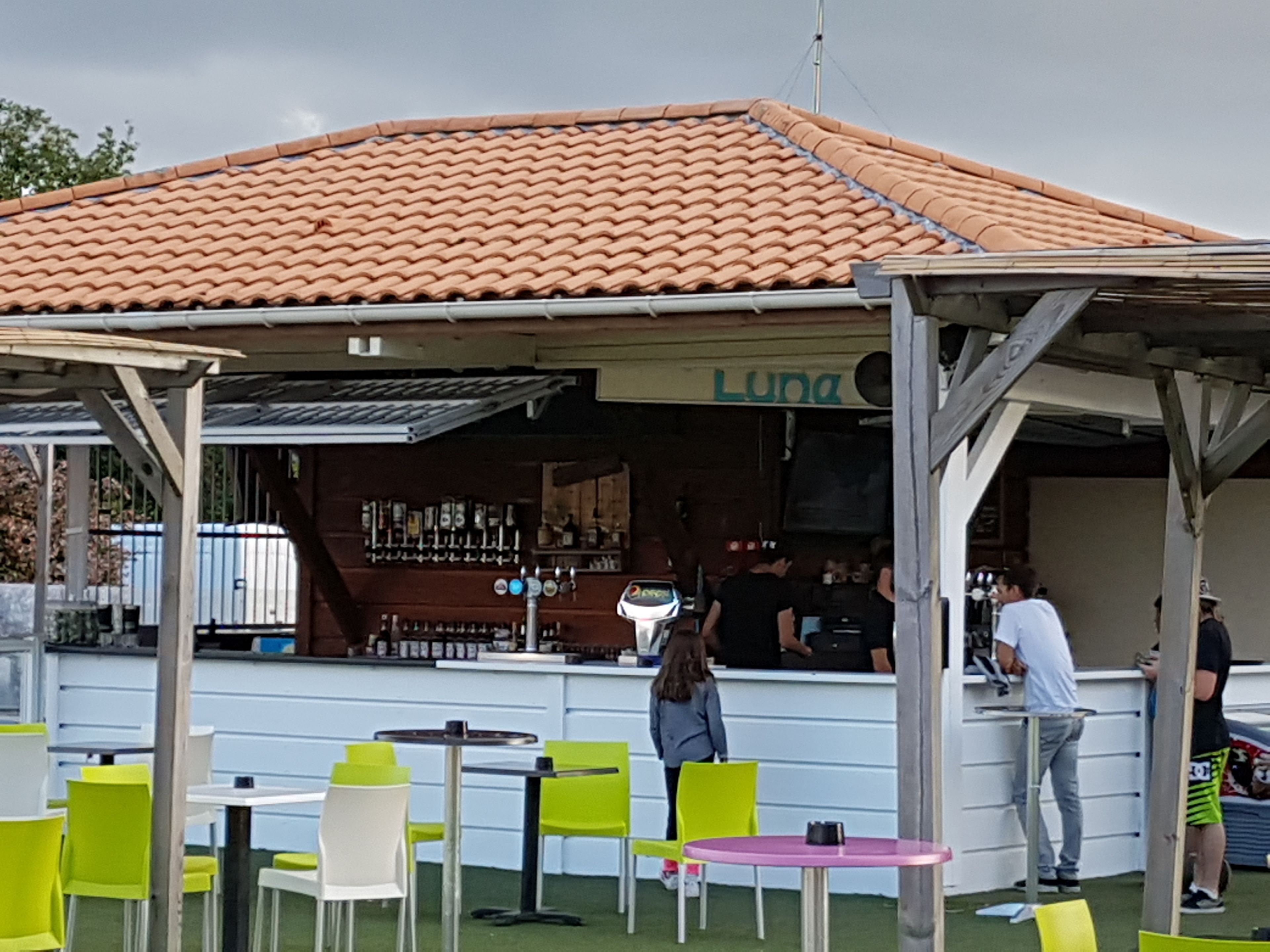 Un espace extérieur aménagé avec des tables et des chaises, un bar doté d’un comptoir et une enseigne sur laquelle on peut lire « Luna ».