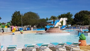 Un área de piscina con sillas de descanso, un tobogán de agua y juguetes inflables.