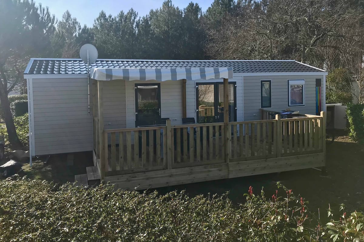 A mobile home with a covered porch, a satellite dish, and a small deck area.