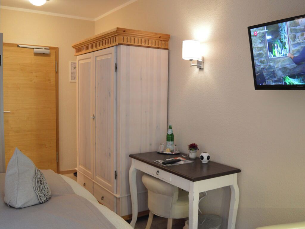 Una camera da letto con un letto, una scrivania, un armadio, una televisione e una lampada a parete.