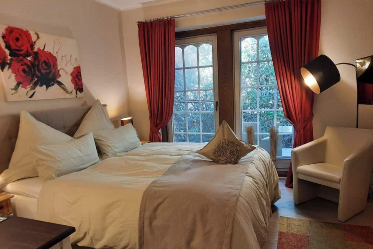 A bedroom with a bed, a chair, a lamp, and a window with curtains.