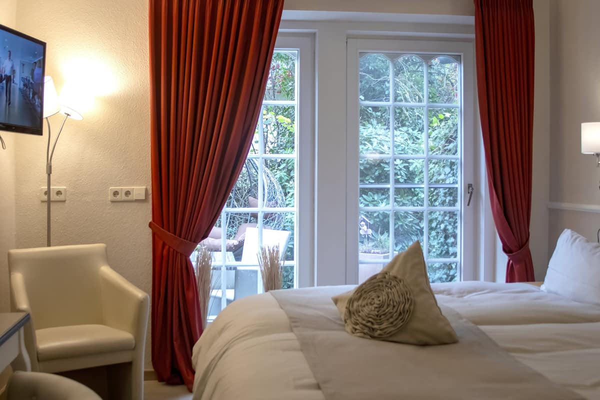 A hotel room with a bed, a chair, a TV, and a window with curtains.