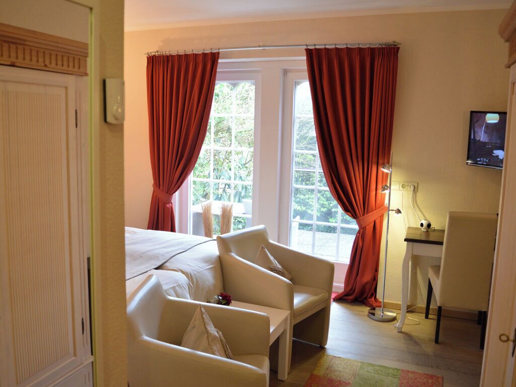 Una camera d'albergo con un letto, due poltrone, una scrivania, un televisore e una finestra con tende.