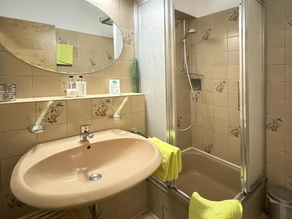 Un baño con lavamanos, espejo, ducha y paredes con azulejos.