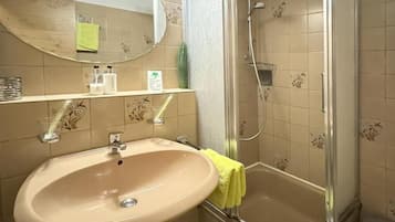 Un baño con lavamanos, espejo, ducha y paredes con azulejos.