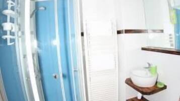 Un baño con cabina de ducha de vidrio, lavabo blanco y suelo de madera.