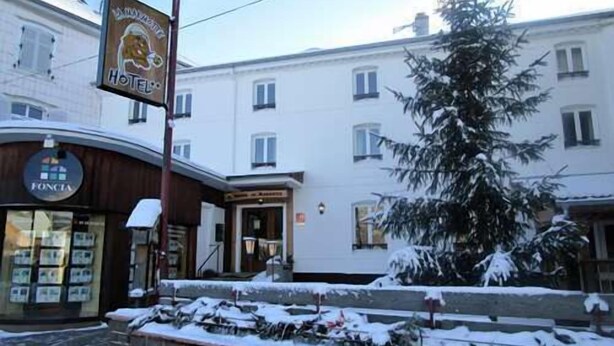 Un hôtel avec une enseigne, un grand sapin de Noël et un mur de pierre à l’avant.