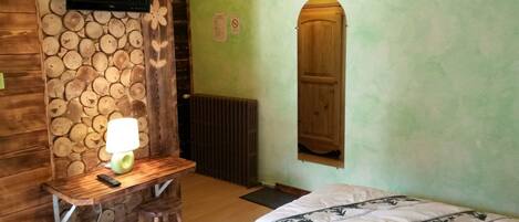 Una habitación con un escritorio de madera, una lámpara, una cama con colcha estampada y una puerta de madera.